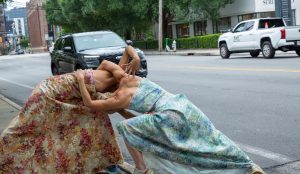 Two dancers in flowing flowered dresses move jointly alongside a roadway